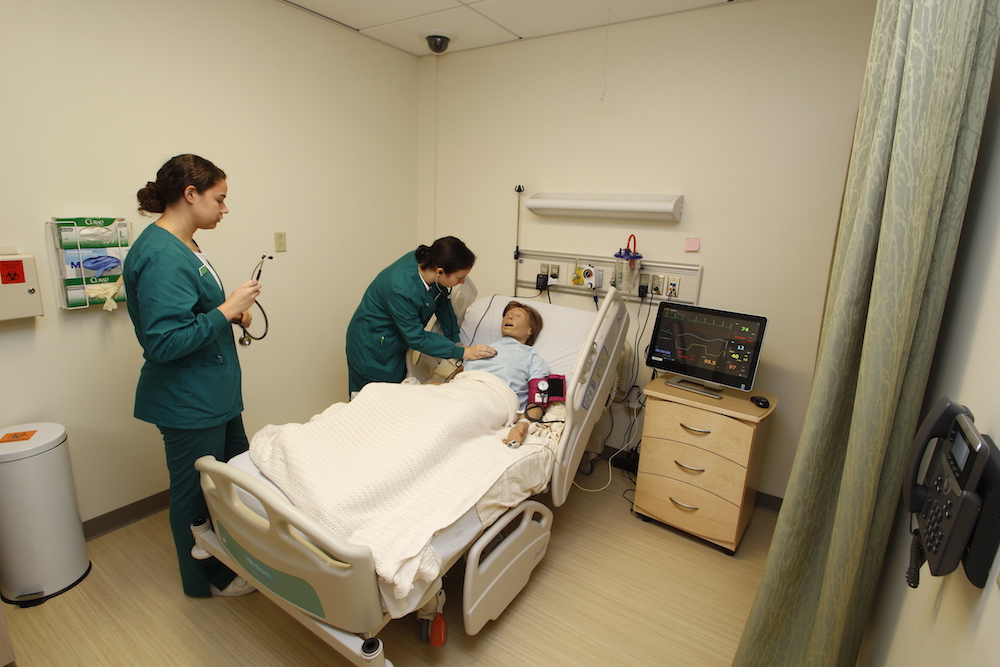 Two healthcare students practice on a patient simulator